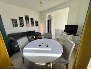 Un salon moderne avec une table à manger ronde, un canapé, un téléviseur et des œuvres d’art accrochées au mur.