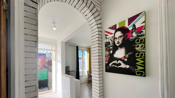 Un interior moderno con un pilar de ladrillo blanco, un ventanal y una obra de arte con un paisaje urbano en la pared.