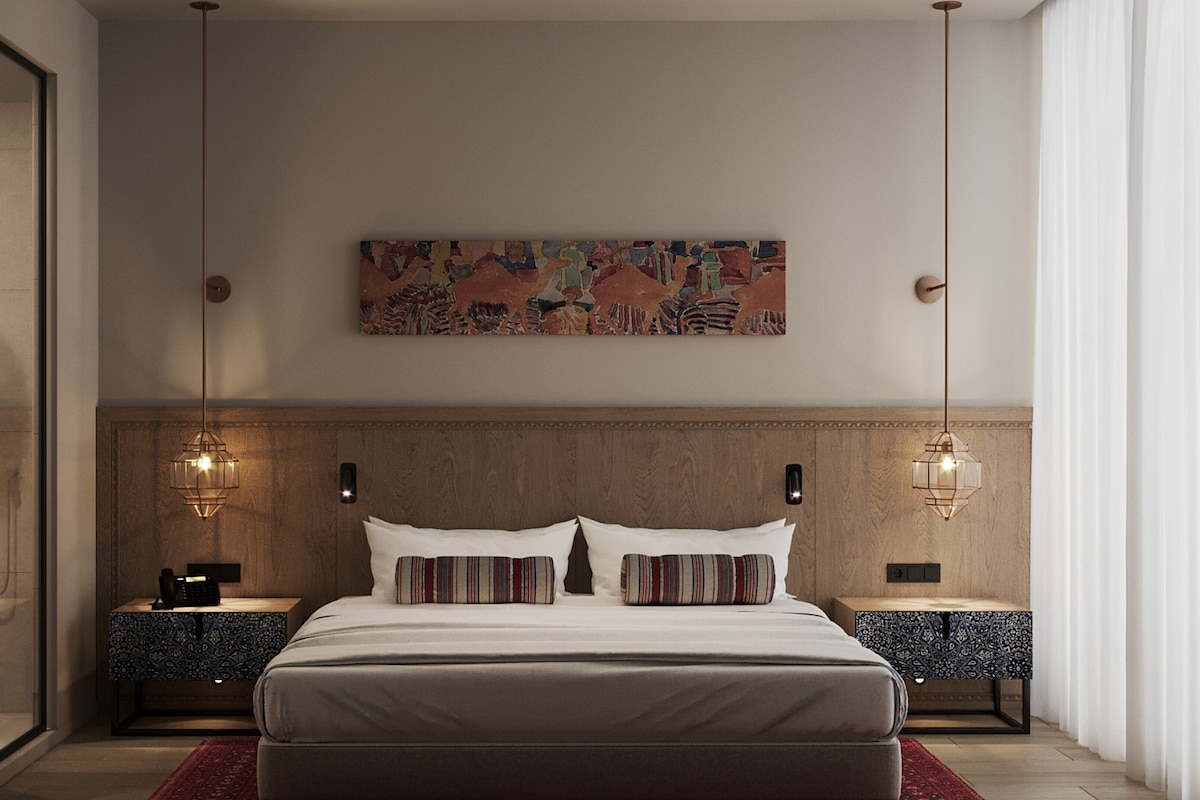Un dormitorio moderno con una cama grande, dos mesitas de noche, una obra de arte colgada en la pared e iluminación colgante.