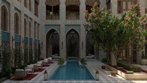 Un patio con piscina, mobiliario y un árbol.