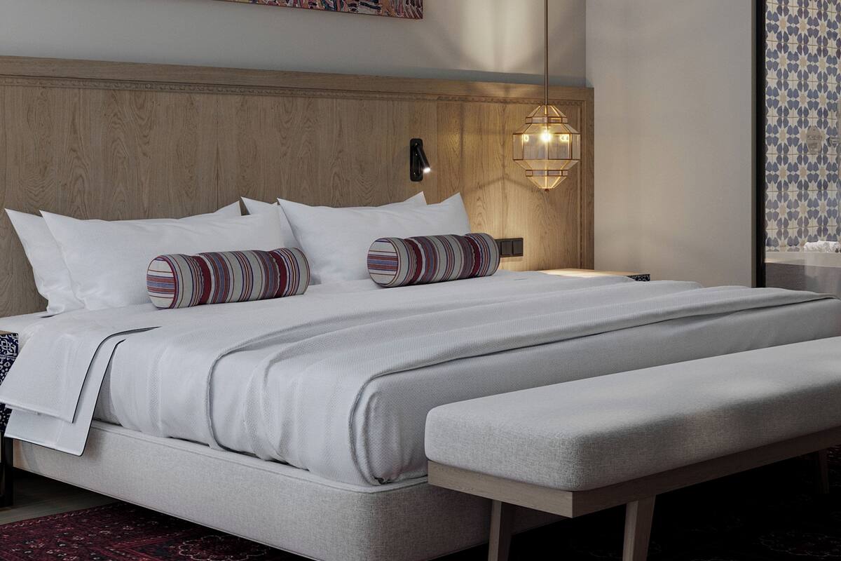 A modern bedroom with a large bed, a bedside table, a bench, and a hanging light fixture.