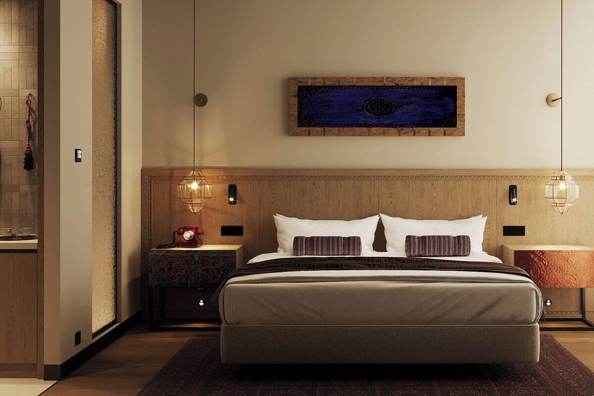 A hotel room with a large bed, two bedside tables, a wall-mounted artwork, and a television.