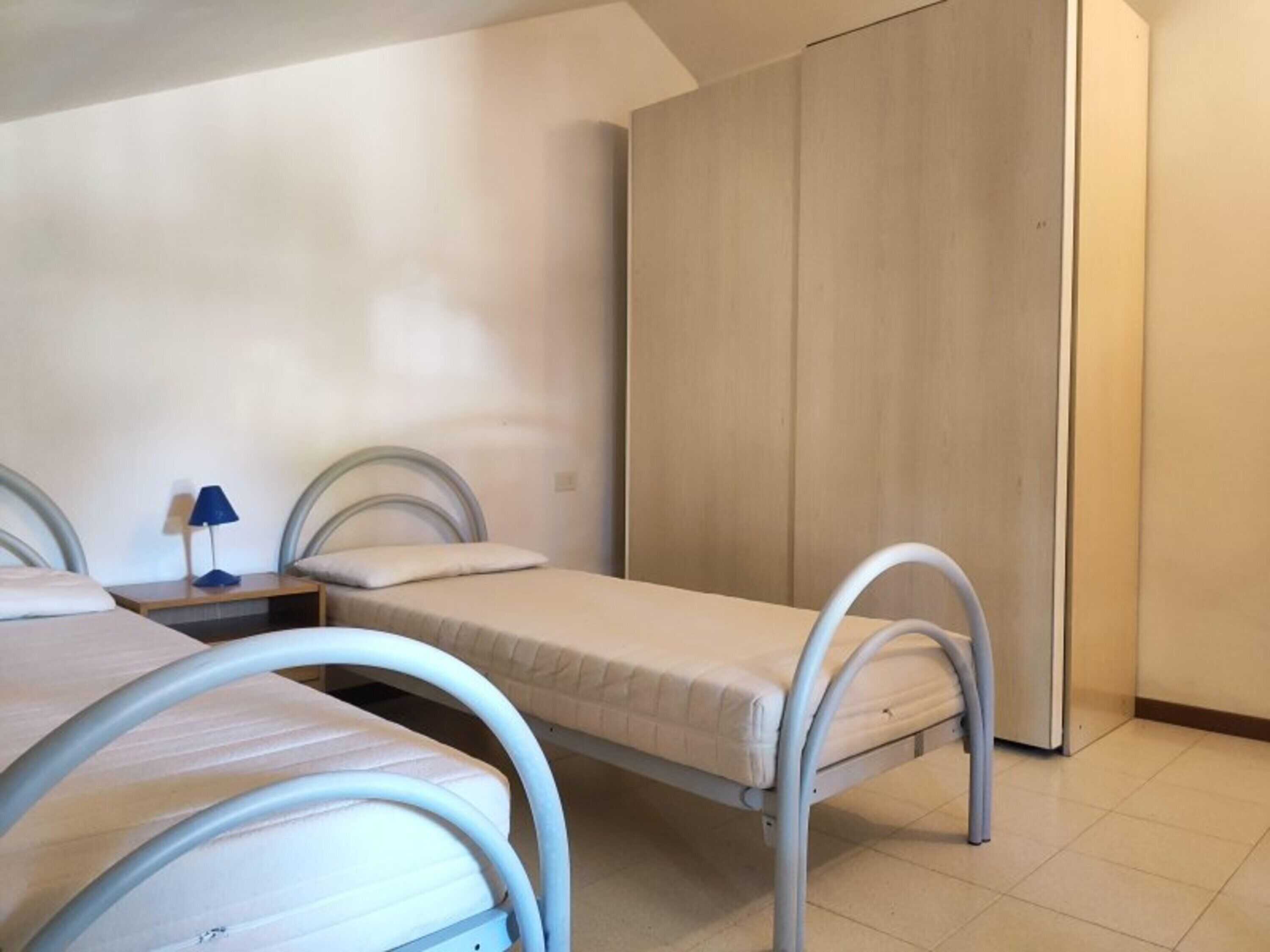 Una habitación con dos camas individuales, una mesita de noche con lámpara y un armario.