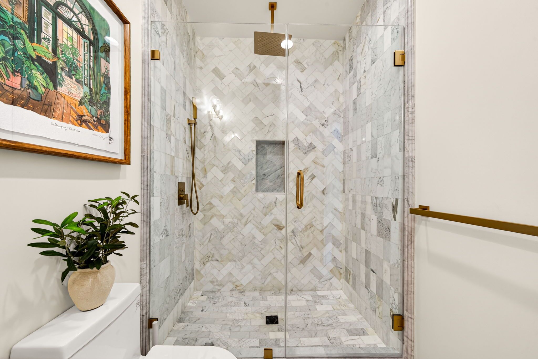 Een moderne badkamer met een visgraatmozaïek, een douche met glazen wand en een ingelijste botanische print aan de muur.