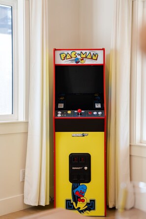 A Pac-Man arcade machine in a room with a window and curtains.