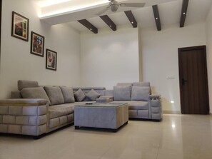 A modern living room with a sectional sofa, a coffee table, and a ceiling fan. - Hotel Heaven and Hills (Kasauli)