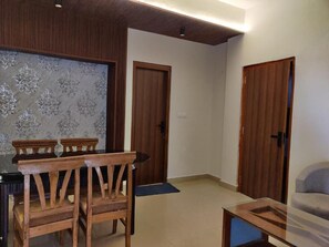 A room with a dining table, chairs, a sofa, and two wooden doors. - Hotel Heaven and Hills (Kasauli)