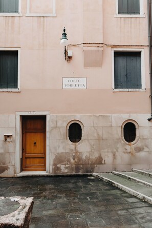 A building with a sign reading 'CORTE TORRETTA,' a wooden door, and a stone-paved courtyard. - Dimora Quadri | 1 min from St. Mark's Square | Romantic Retreat for Couples (Venezia)