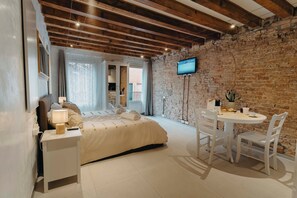 A bedroom with a bed, bedside table, lamp, TV, and a dining area with chairs and a table. - Dimora Quadri | 1 min from St. Mark's Square | Romantic Retreat for Couples (Venezia)