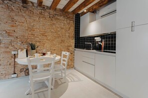 Une cuisine avec des meubles blancs, un mur en briques et un pare-feu en carreaux.