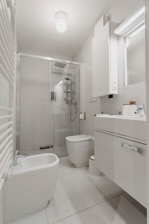 Une salle de bain moderne dotée d’une douche à parois de verre, de toilettes blanches, d’un bidet et d’un meuble-lavabo avec un miroir.
