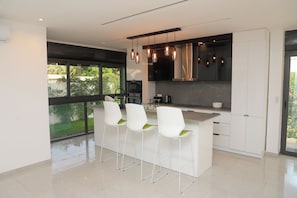 Une cuisine moderne avec des tabourets de bar blancs, une grande fenêtre et une vue sur la verdure à l’extérieur.