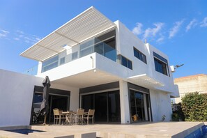 Une maison moderne à deux étages, dotée d’un patio couvert, d’une piscine et d’une grande entrée avec une porte en verre.