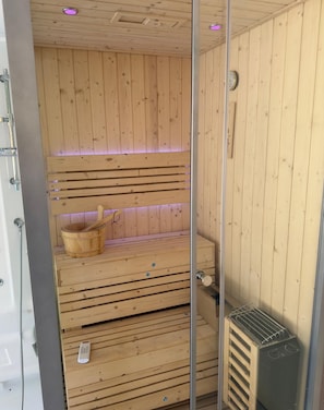 A wooden sauna with benches, a wooden bucket, and a heater. - Villa escape and spa (Limoges)