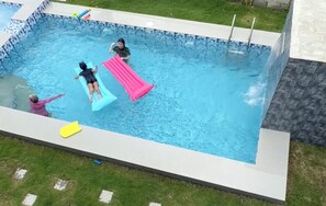 Une piscine rectangulaire bordée de carreaux, avec une pelouse devant et un mur de pierre sur un côté.