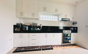 Une cuisine avec des meubles blancs, un plan de travail noir, une cuisinière et un four encastré.