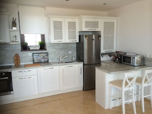 Een moderne keuken met witte kasten, een roestvrijstalen koelkast, een magnetron en een klein eiland met barkrukken.