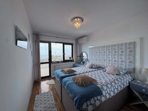 Een slaapkamer met twee bedden, een groot raam, een plafondlamp en een hoofdbord met een patroon.