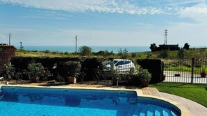 Une piscine avec vue sur la mer, entourée de verdure et délimitée par une clôture.