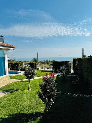 A residential property with a swimming pool, a well-maintained lawn, and a view of the sea.