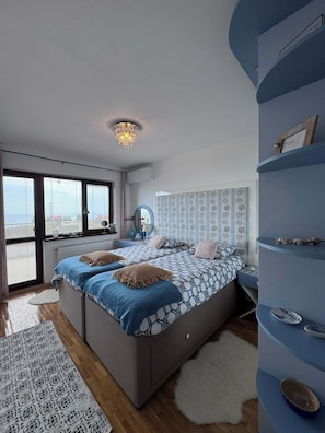 A modern bedroom with a large bed, built-in shelving, and a view through the window.