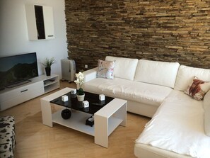 Un salon moderne avec un mur en pierre, un canapé blanc et une table basse en verre agrémentée d’objets décoratifs.