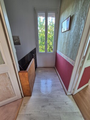 A narrow hallway with a wooden floor, a door with a window, and a wall with a framed picture. - Fourasine family home 300m from the beach (Fouras)
