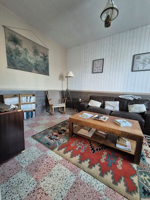 A living room with a coffee table, sofa, patterned rug, bookshelf, and a painting on the wall. - Fourasine family home 300m from the beach (Fouras)