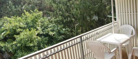 A balcony with white chairs and a table, overlooking dense greenery.