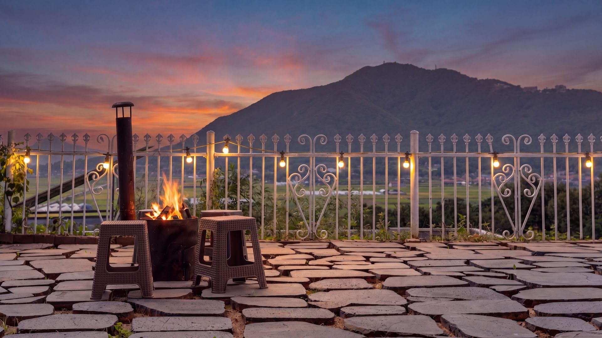An outdoor seating area with a fire feature, a metal fence, and a view of a mountain.