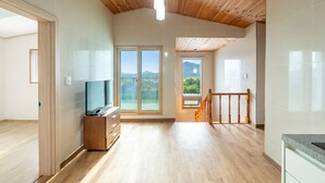 Una habitación amplia con techo de madera, un televisor sobre un mueble de madera, una puerta corrediza de vidrio que da a un balcón y una zona de cocina con encimera de granito.