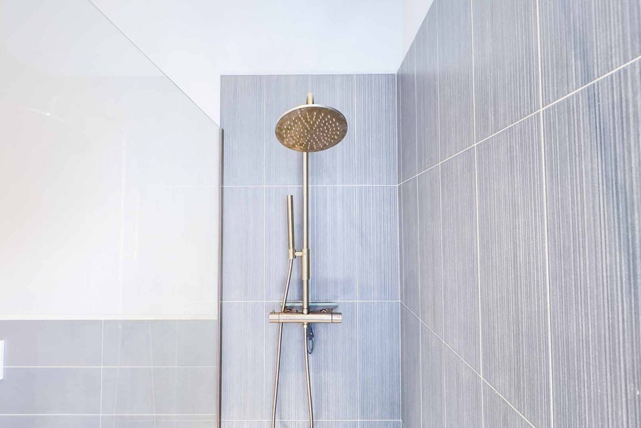 Een moderne douche met een ronde douchekop, een handdouche en een bedieningspaneel aan de muur.