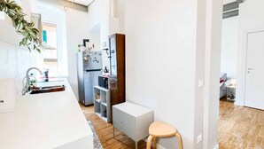 Une cuisine compacte avec un plan de travail blanc, un réfrigérateur encastré et un petit tabouret.