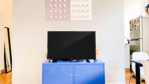 Une chambre moderne avec un téléviseur à écran plat posé sur un meuble bleu, des œuvres d’art murales et un réfrigérateur.