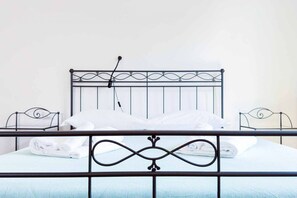 Een bed met een metalen hoofdbord, witte beddengoed en een handdoekrek.