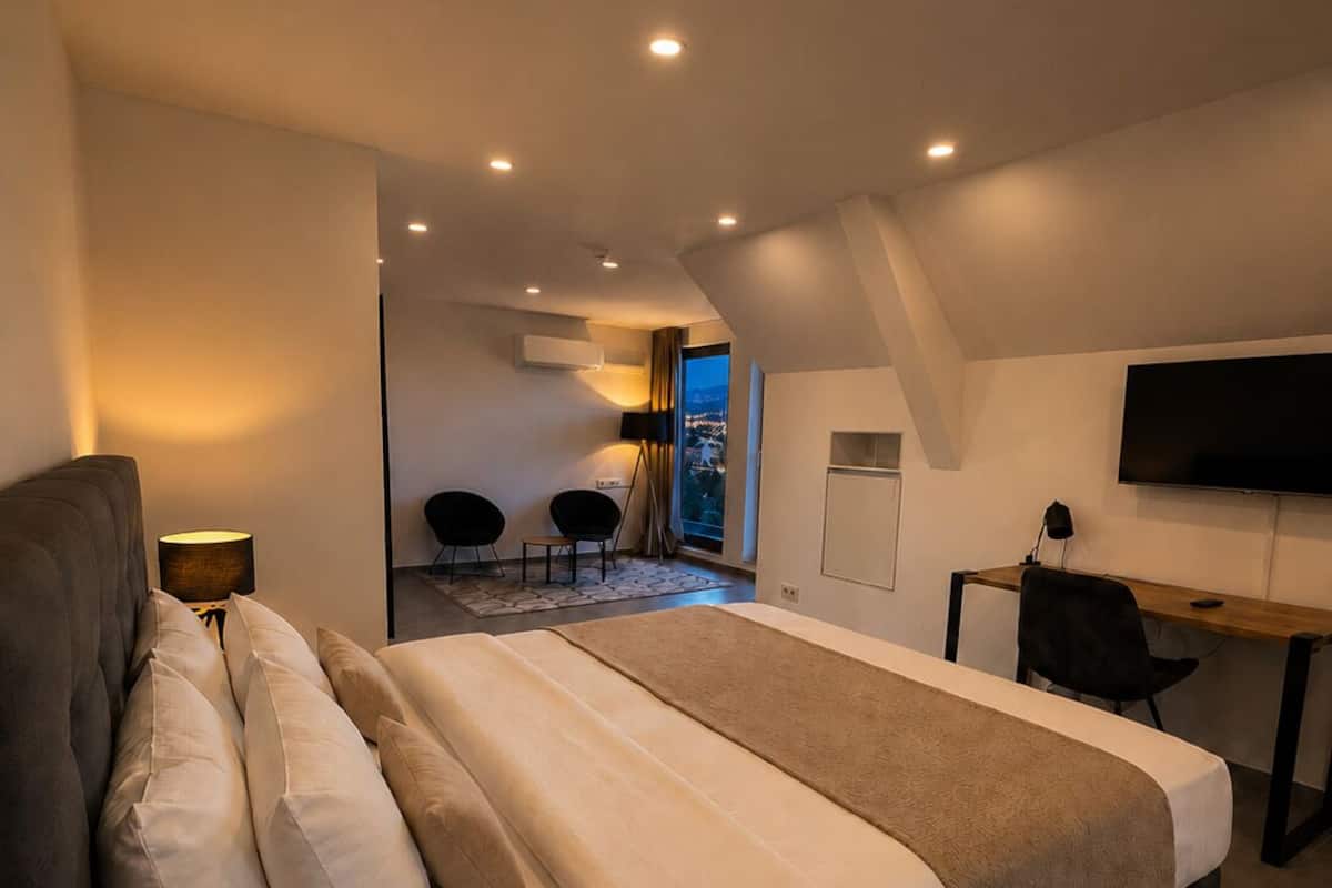 Une chambre moderne avec un grand lit, un bureau, une télévision et une vue sur la ville la nuit.