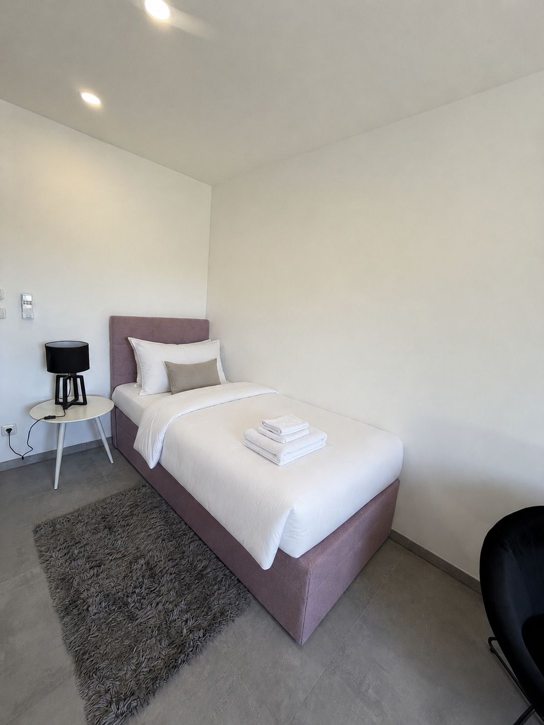Un dormitorio moderno con una cama, una mesita de noche, una lámpara y una alfombra.