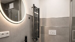 Un baño moderno con un lavamanos negro, un espejo redondo con iluminación, una toalla, un inodoro y una zona de ducha.