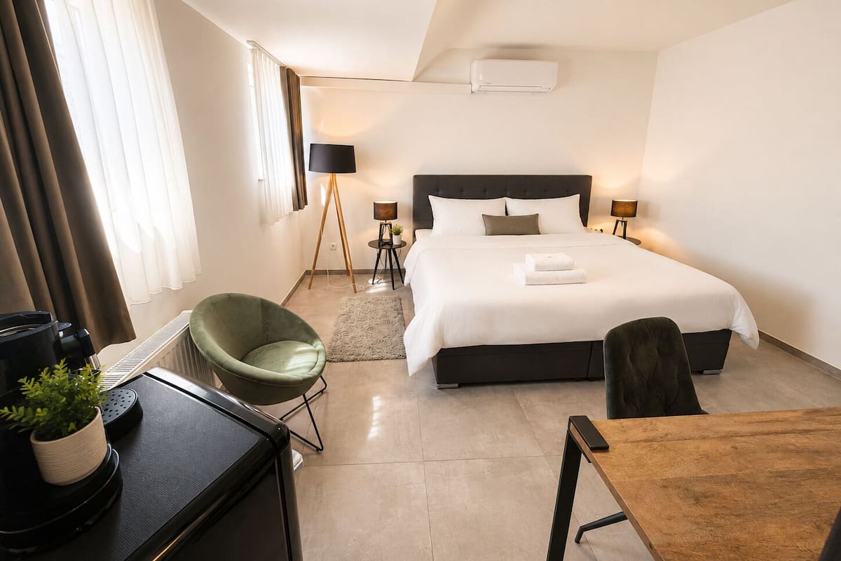 Une chambre d’hôtel avec un lit, un bureau, une chaise, une lampe et un radiateur.