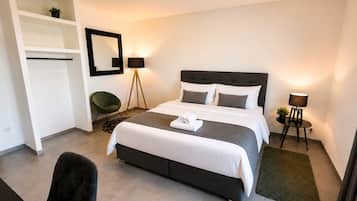 A modern bedroom with a bed, bedside lamps, a chair, and a small table with a plant.