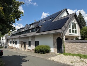 Una casa de dos pisos con paneles solares en el techo, fachada de ladrillo y entrada para vehículos.