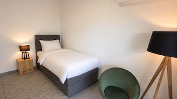 A bedroom with a bed, a bedside lamp, a green chair, and an air conditioning unit.