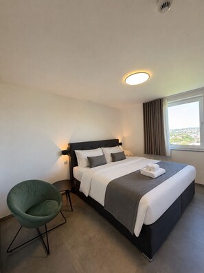 Een hotelkamer met een bed, een stoel, een raam met gordijnen en uitzicht op de stad.