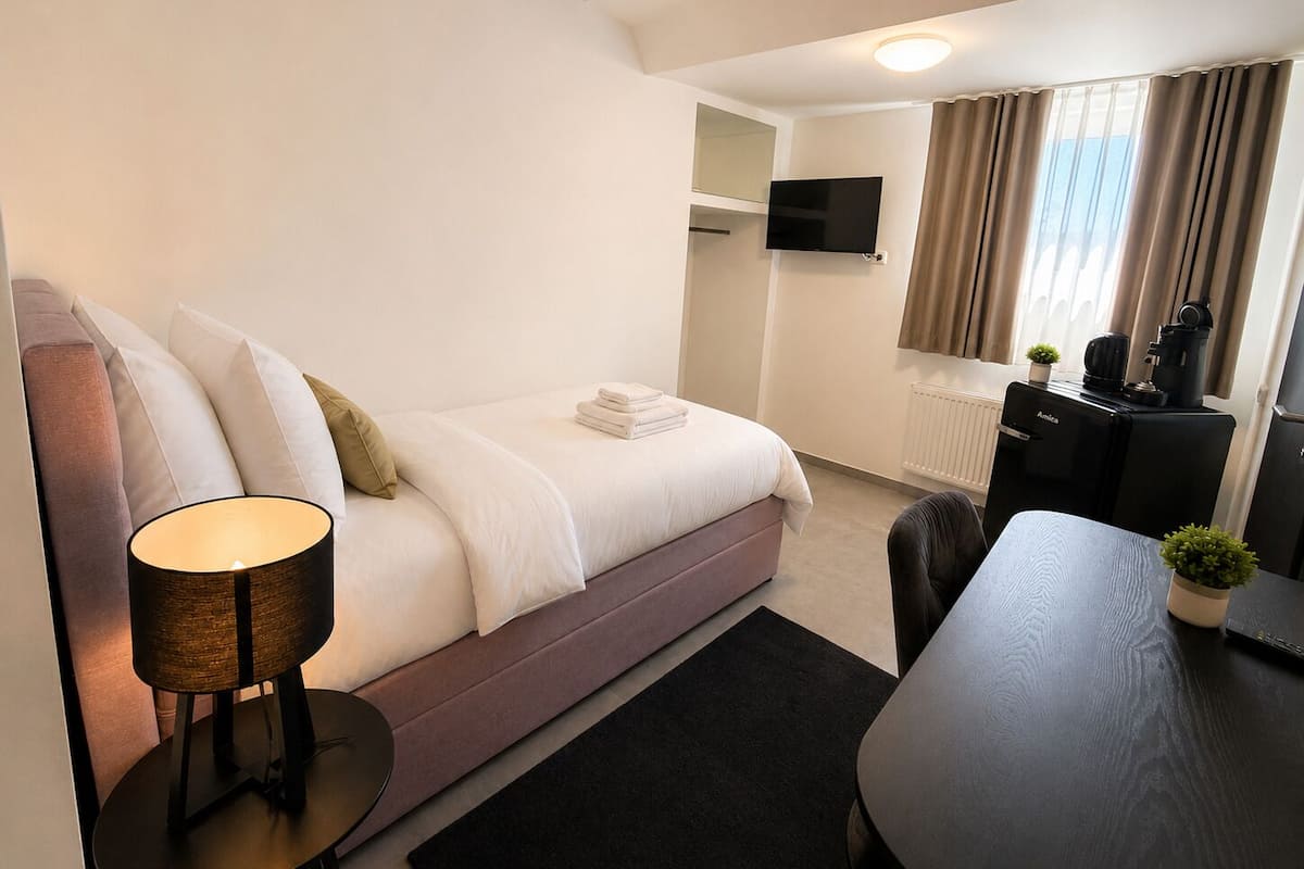 Une chambre d’hôtel moderne équipée d’un lit, d’un bureau, d’une chaise, d’une lampe, d’une télévision et d’une machine à café.