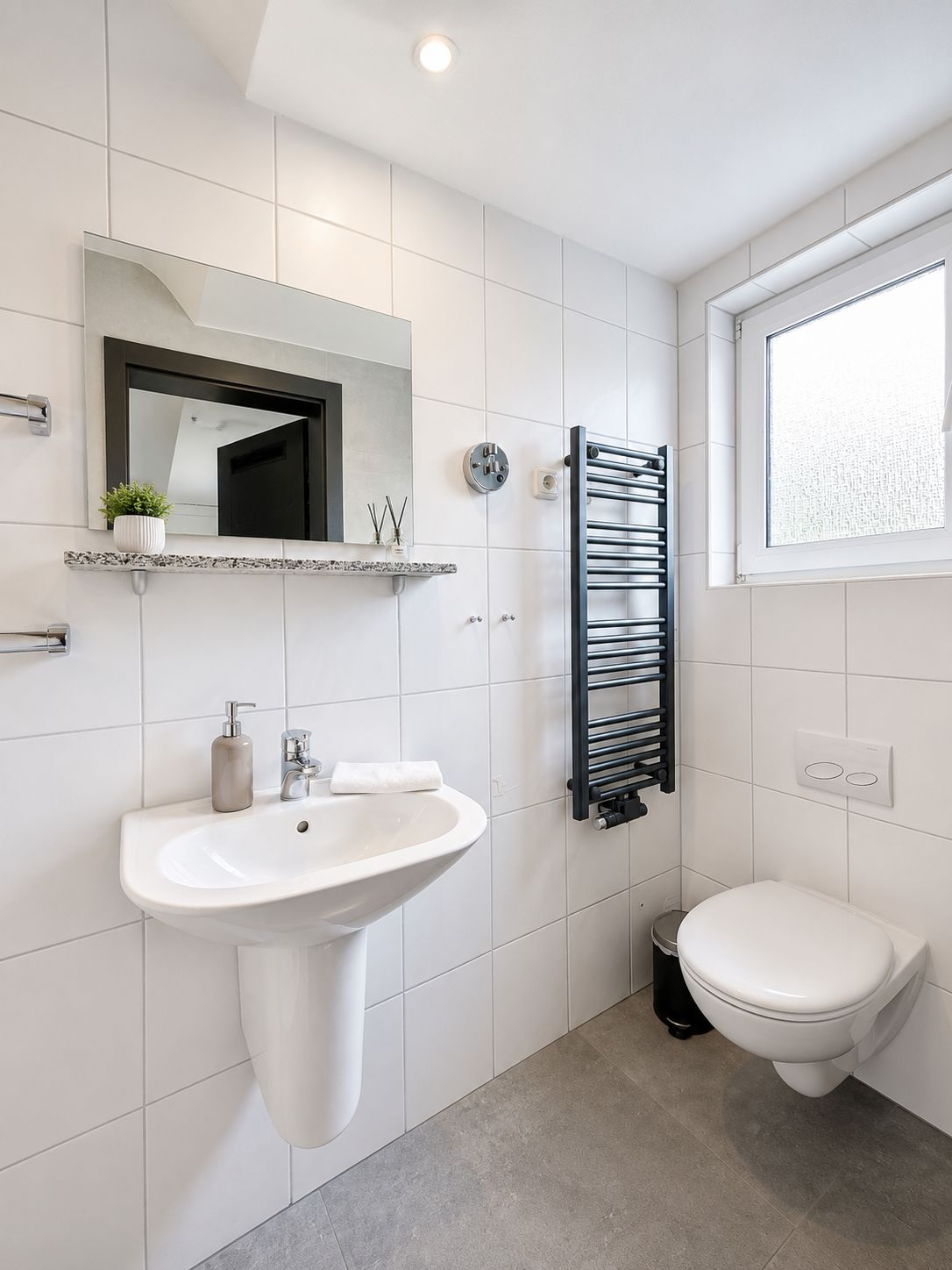 A modern bathroom with a white sink, a mirror, a towel rack, and a toilet.