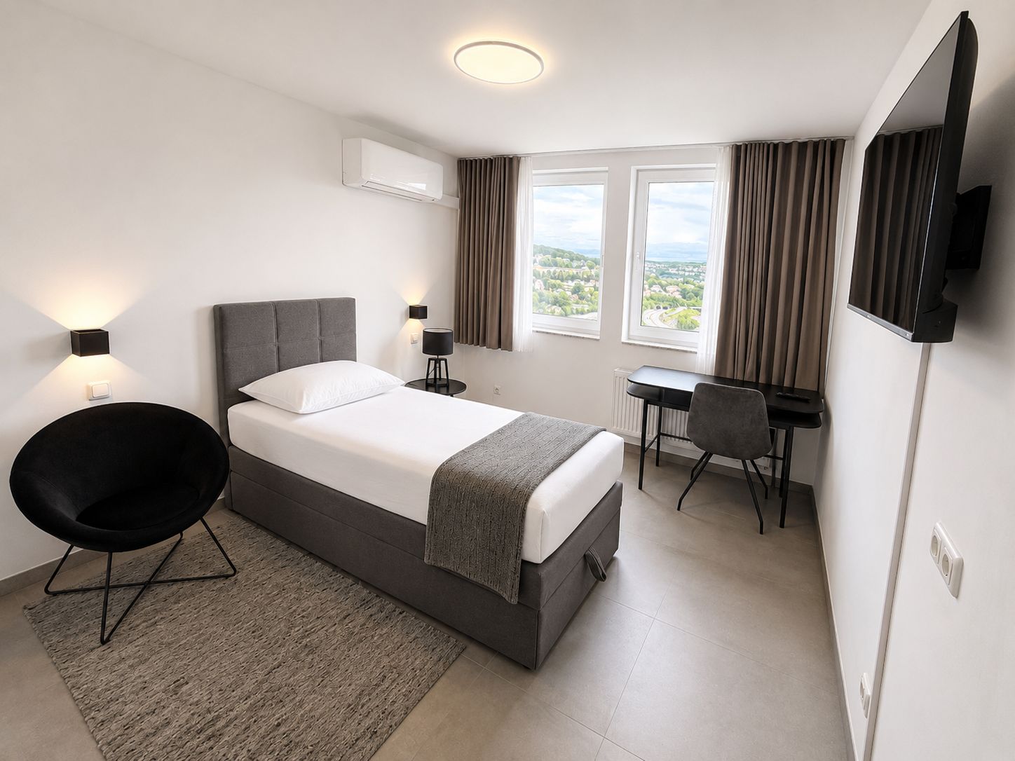 A modern hotel room with a bed, desk, chair, and a TV.