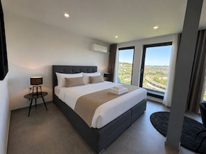 Een moderne hotelkamer met een groot bed, een klein tafeltje, een lamp en uitzicht op de stad.