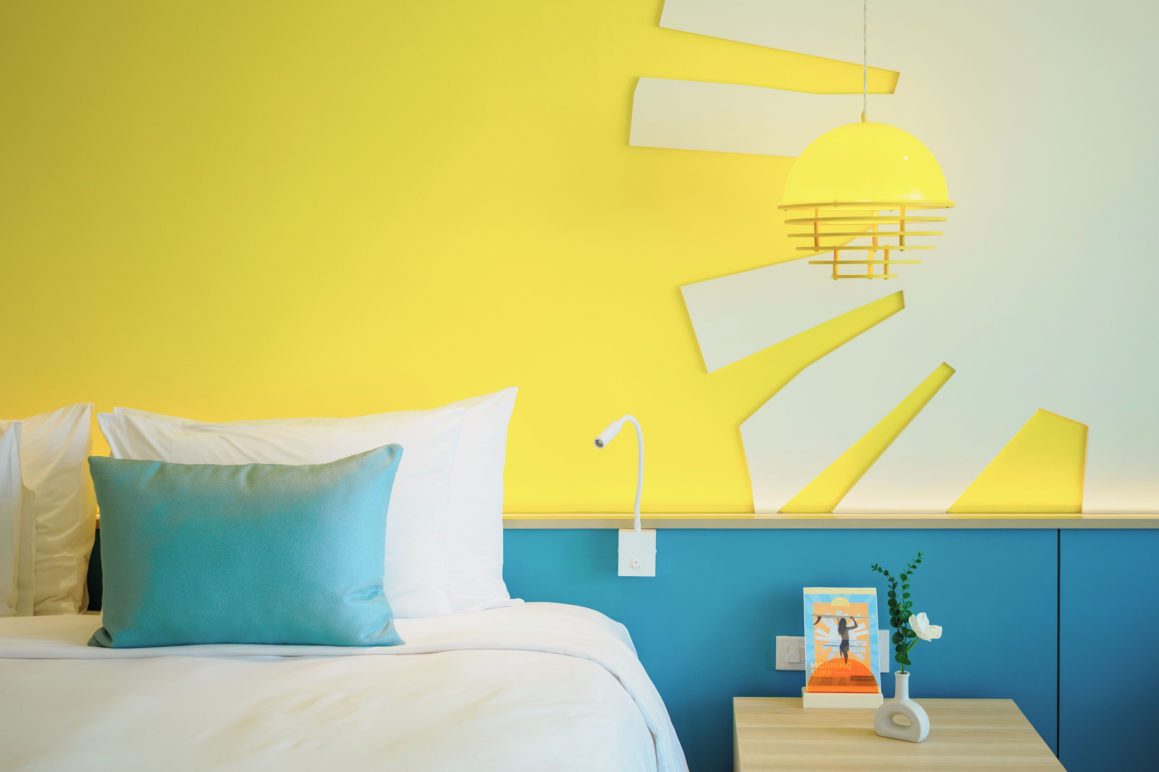 A hotel room with a bed, a nightstand, a wall-mounted lamp, and a framed picture.