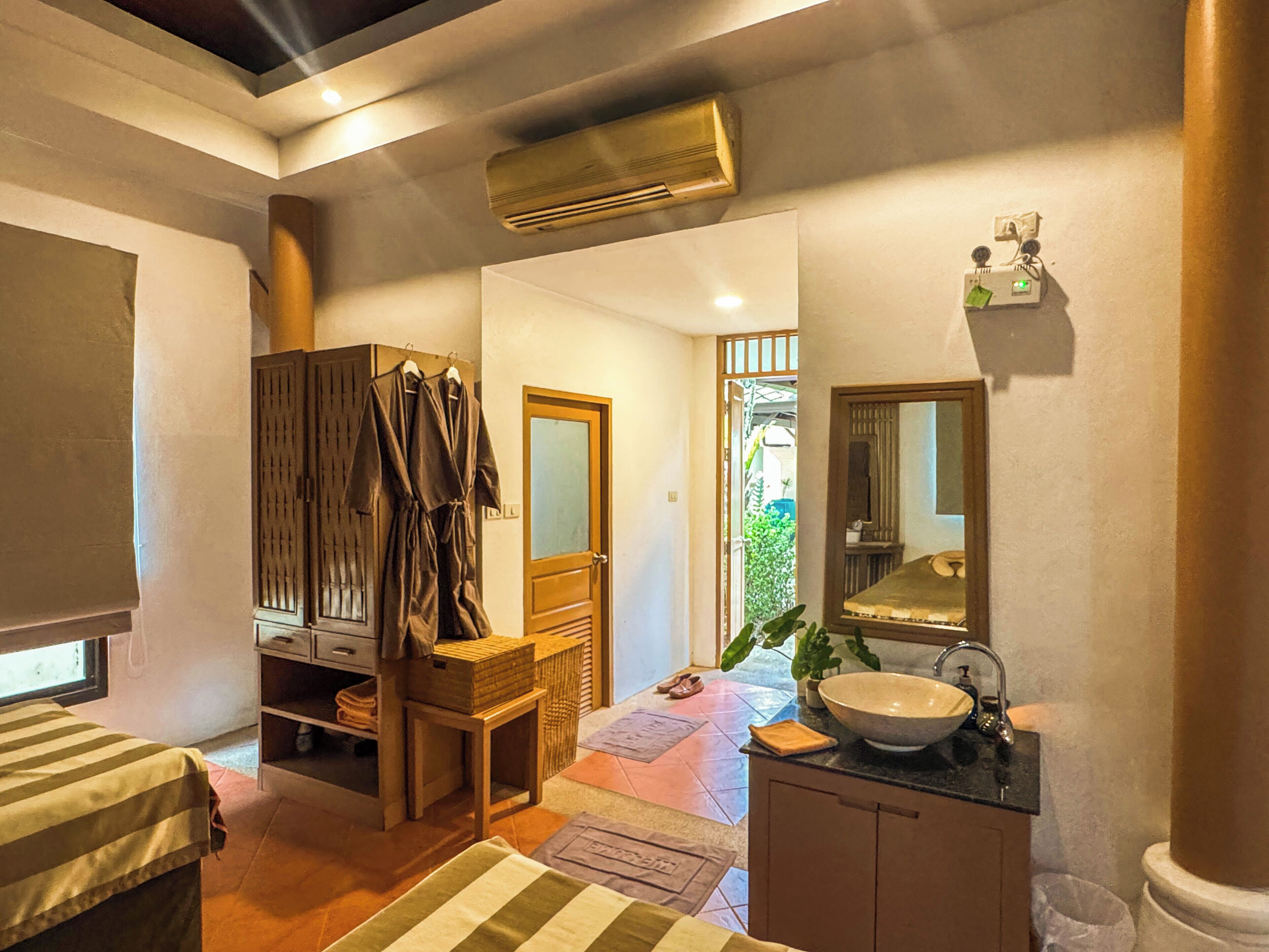A hotel room with a bed, a wooden cabinet, a mirror, a sink, and an air conditioning unit.