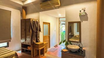 A hotel room with a bed, a wooden cabinet, a mirror, a sink, and an air conditioning unit.
